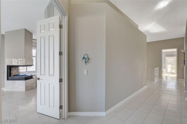 corridor with an upstairs landing, baseboards, and light tile patterned flooring