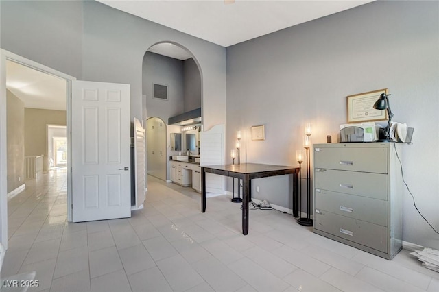 office area featuring arched walkways, visible vents, a towering ceiling, and baseboards