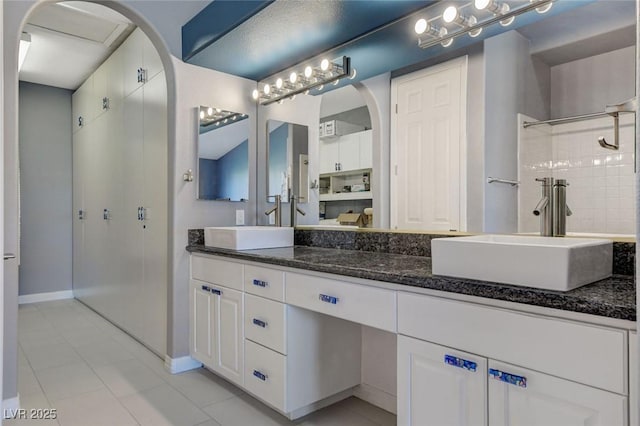 bathroom featuring double vanity, a tile shower, a sink, and tile patterned floors