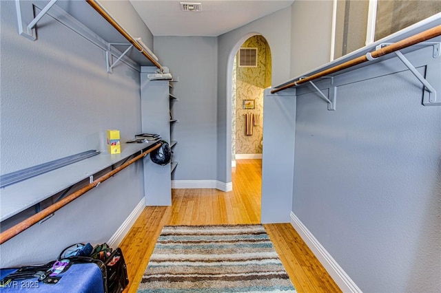 walk in closet with arched walkways, wood finished floors, and visible vents