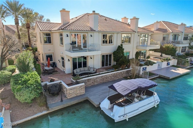 rear view of property featuring a tiled roof, a water view, a balcony, and stucco siding