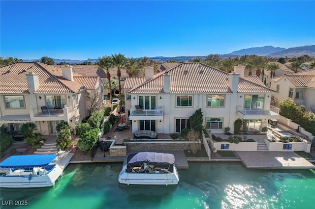 rear view of property with a tiled roof, a water and mountain view, a residential view, a chimney, and stucco siding