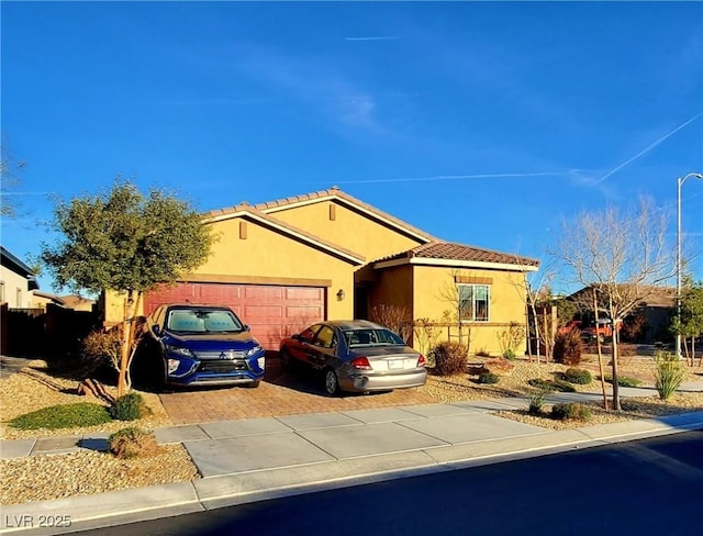 view of front facade with a garage, decorative driveway, a tiled roof, and stucco siding