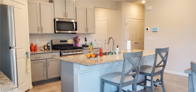 7910 Shimmery St, North Las Vegas, NV 89084 - kitchen featuring stainless steel appliances, a breakfast bar area, gray cabinets, and light stone counters