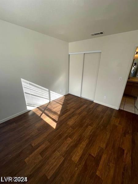 unfurnished bedroom featuring a closet, visible vents, dark wood finished floors, and baseboards