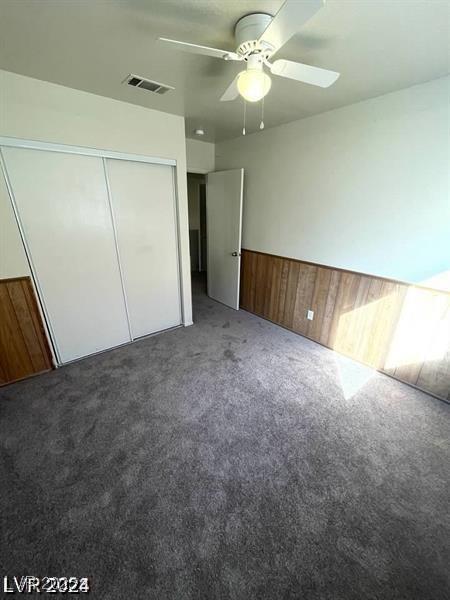 unfurnished bedroom with a wainscoted wall, wood walls, visible vents, a closet, and dark colored carpet