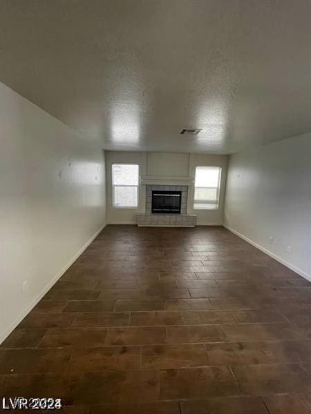 unfurnished living room featuring baseboards, visible vents, a tiled fireplace, and a textured ceiling