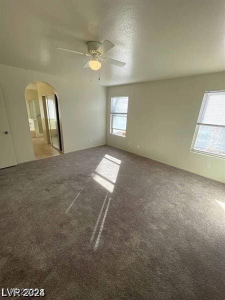 unfurnished room featuring a ceiling fan, arched walkways, and carpet flooring