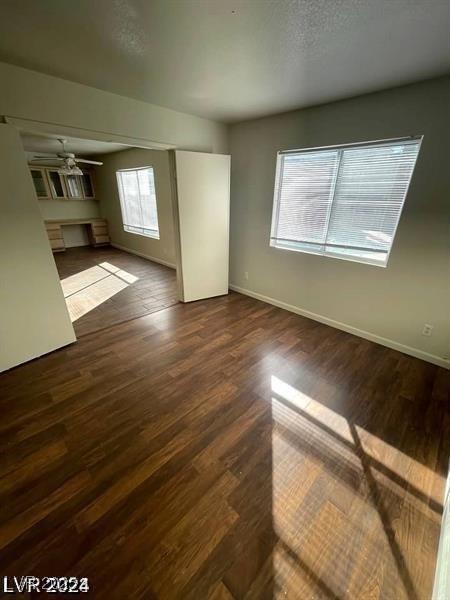 unfurnished living room with dark wood-style floors, ceiling fan, a textured ceiling, and baseboards