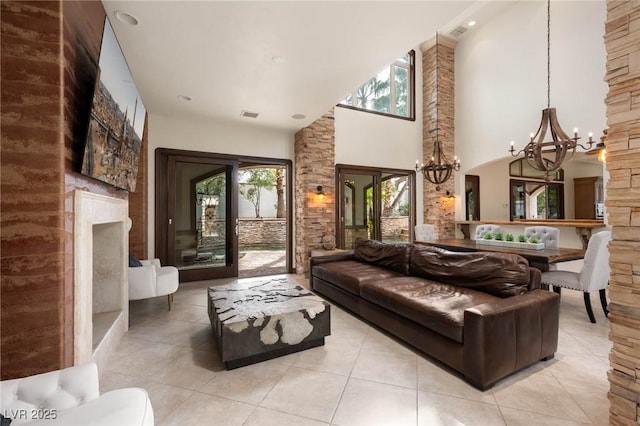 living area with a fireplace, a notable chandelier, light tile patterned floors, visible vents, and a towering ceiling