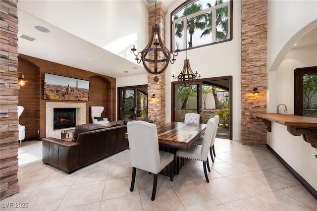 dining room with a lit fireplace, light tile patterned flooring, a towering ceiling, and visible vents