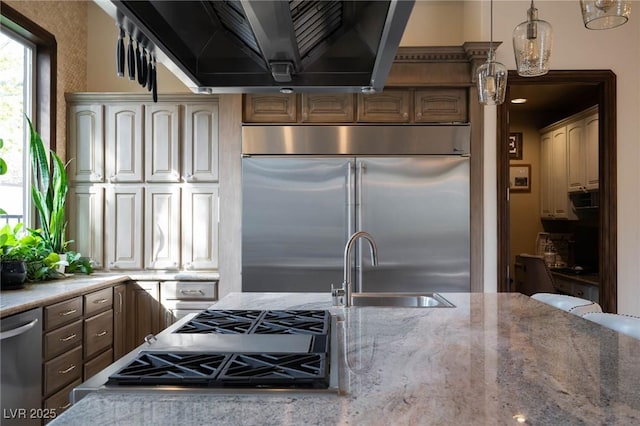 kitchen with appliances with stainless steel finishes, a sink, light stone counters, and extractor fan