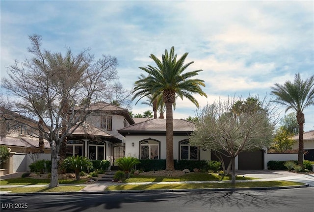 mediterranean / spanish-style house with a garage, concrete driveway, a tile roof, fence, and stucco siding