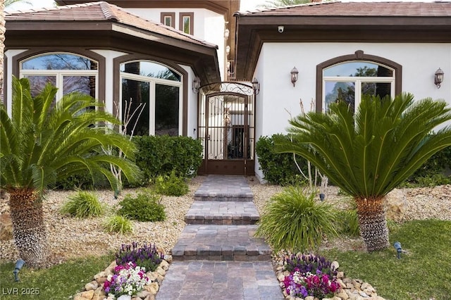 entrance to property featuring a tile roof, a gate, and stucco siding