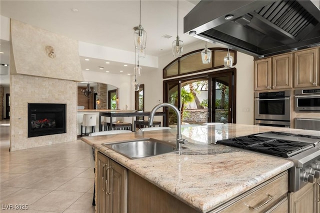 kitchen featuring light stone counters, decorative light fixtures, a sink, an island with sink, and extractor fan