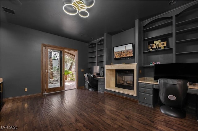 unfurnished office featuring baseboards, dark wood-type flooring, built in shelves, built in desk, and a multi sided fireplace