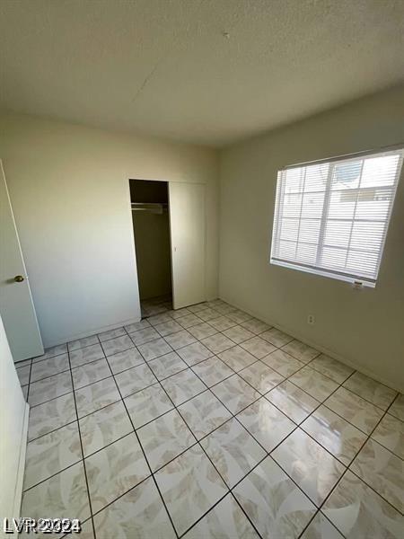 unfurnished bedroom with a textured ceiling, light tile patterned floors, and a closet