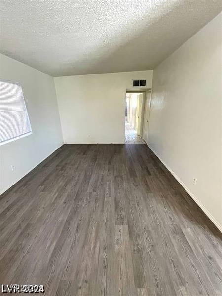 unfurnished room featuring a textured ceiling, visible vents, and dark wood-style flooring