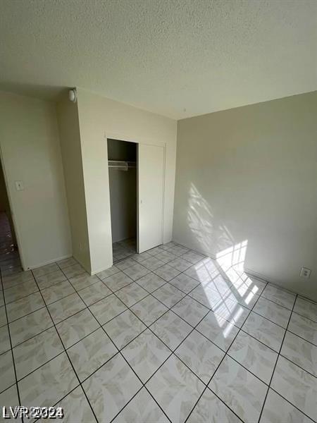 unfurnished bedroom featuring a closet, a textured ceiling, and light tile patterned floors