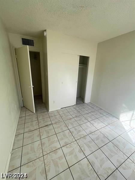 unfurnished bedroom with light tile patterned floors, a textured ceiling, visible vents, and a closet