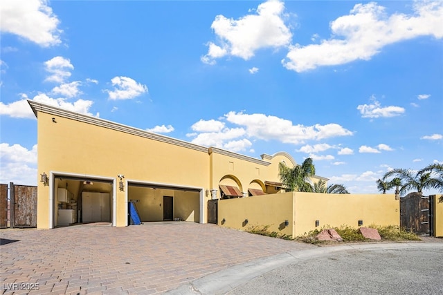 view of front of house with a gate, decorative driveway, fence, and stucco siding