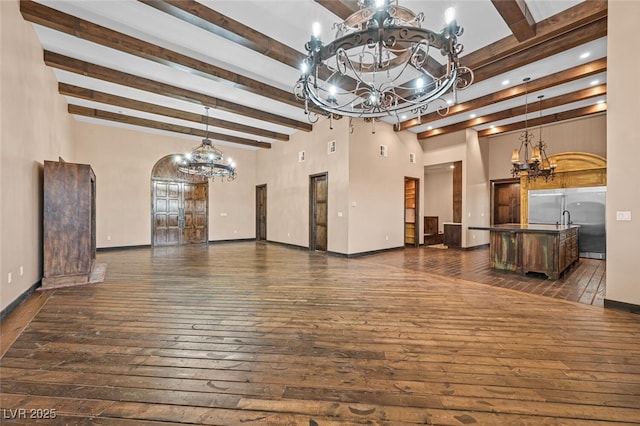 unfurnished living room featuring a chandelier, arched walkways, baseboards, dark wood-style floors, and beamed ceiling