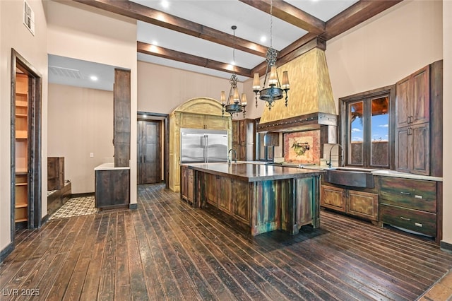 kitchen featuring a sink, visible vents, dark wood-style floors, stainless steel built in refrigerator, and a center island with sink