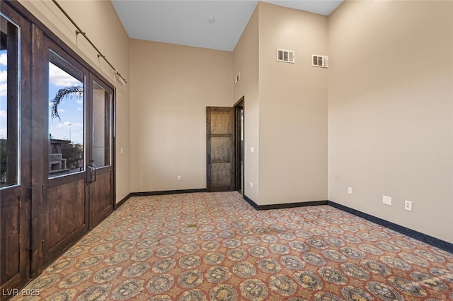 empty room featuring a towering ceiling, baseboards, and visible vents