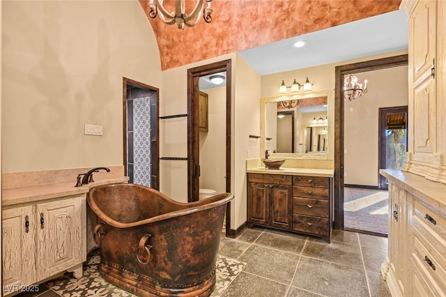 bathroom featuring stone tile floors, baseboards, a freestanding bath, and vanity