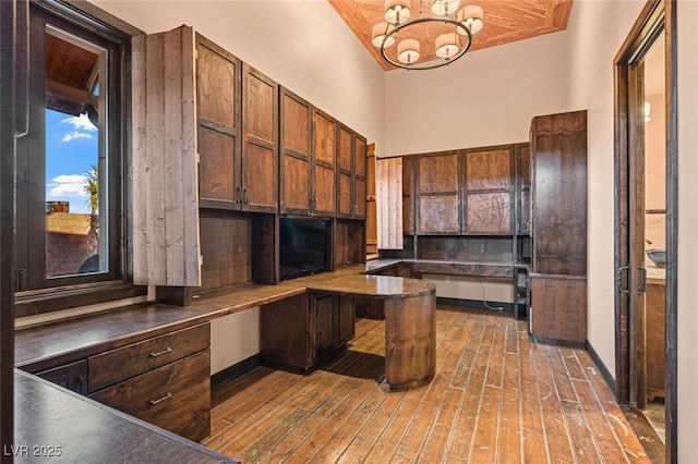 kitchen with a chandelier, dark wood-type flooring, a high ceiling, baseboards, and dark countertops