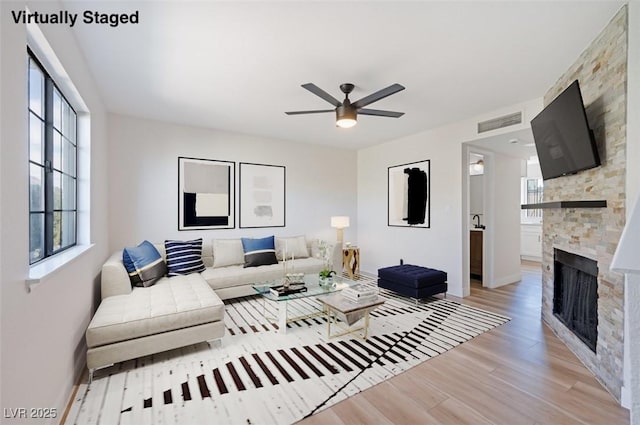 living room with a stone fireplace, light wood-type flooring, visible vents, and a healthy amount of sunlight