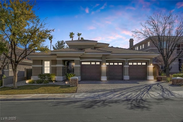 prairie-style home featuring a garage, decorative driveway, and stucco siding