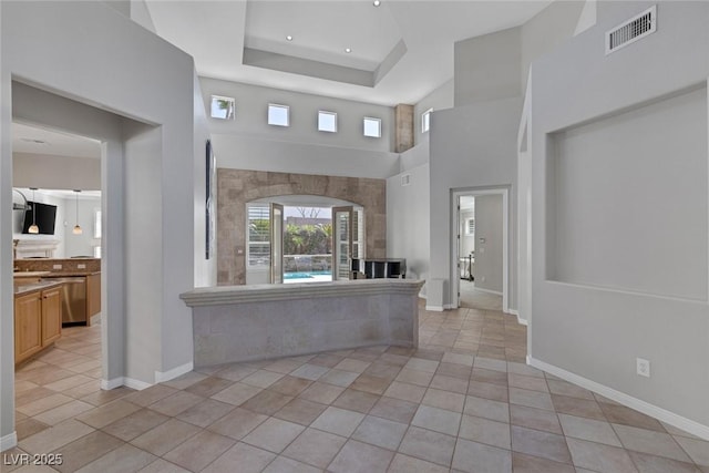 interior space with baseboards, visible vents, a tray ceiling, and light tile patterned flooring