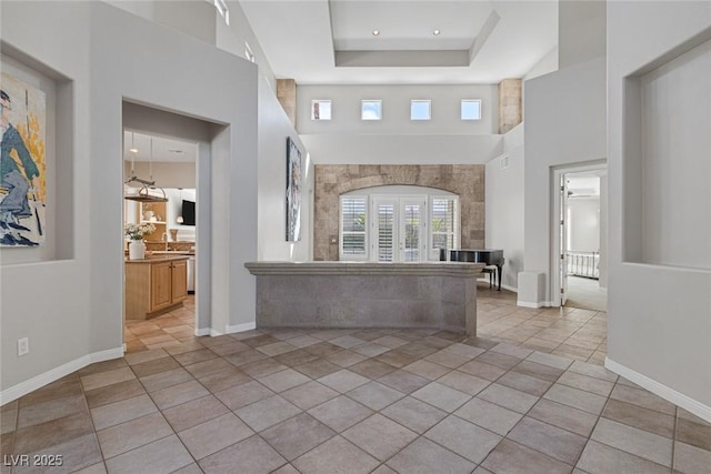 foyer with light tile patterned floors, baseboards, a high ceiling, and a tray ceiling