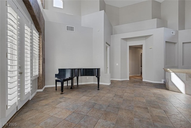 unfurnished living room featuring a high ceiling, visible vents, and baseboards