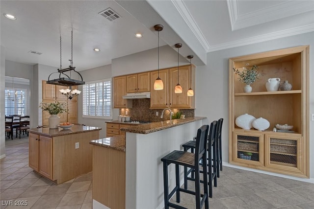 kitchen with visible vents, dark stone counters, decorative light fixtures, a peninsula, and under cabinet range hood