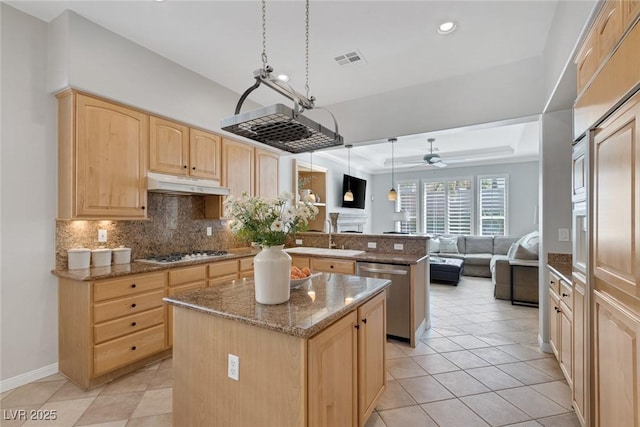 kitchen with a raised ceiling, hanging light fixtures, a kitchen island, dishwasher, and under cabinet range hood