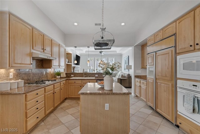 kitchen featuring a center island, hanging light fixtures, built in appliances, light brown cabinetry, and under cabinet range hood