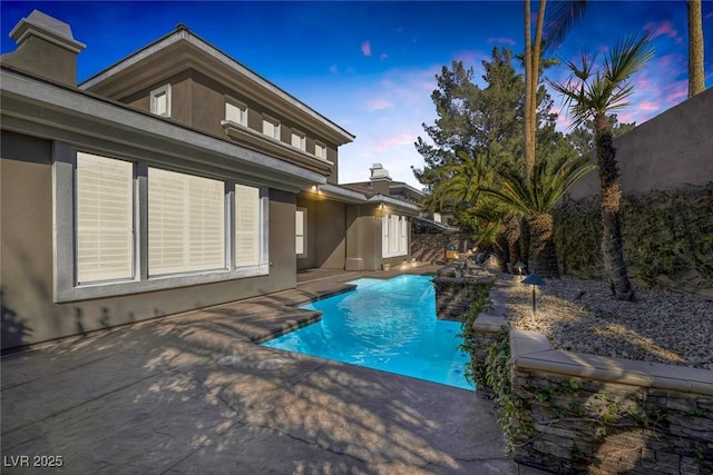 back of property at dusk with a chimney, fence, an outdoor pool, and stucco siding