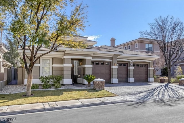 prairie-style home with decorative driveway, a tile roof, stucco siding, an attached garage, and a front lawn