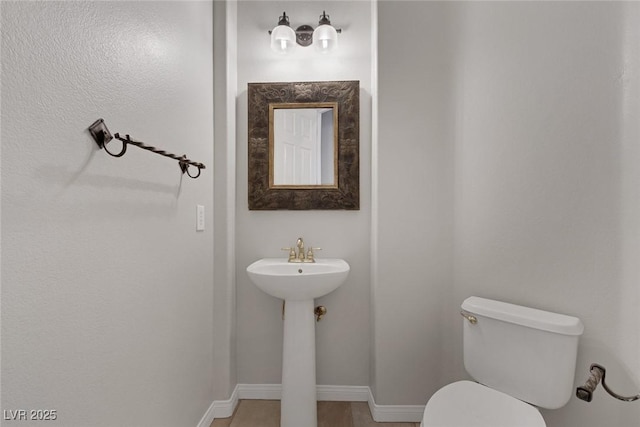 half bath featuring a sink, toilet, and baseboards