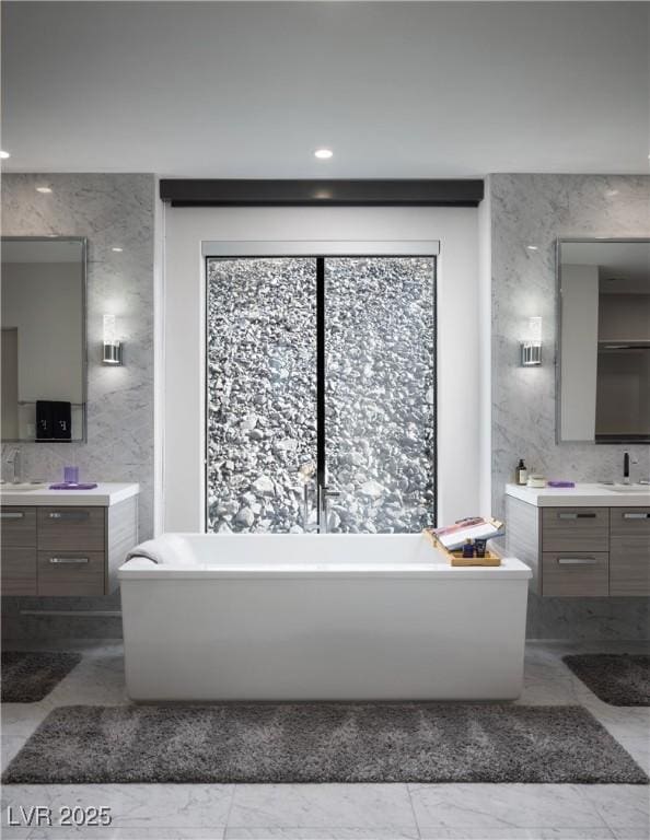 full bathroom featuring two vanities, marble finish floor, a healthy amount of sunlight, and a sink