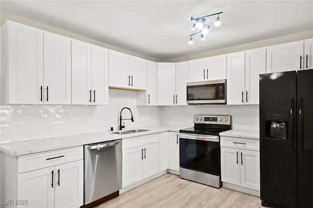 kitchen featuring light wood-style flooring, appliances with stainless steel finishes, white cabinets, a sink, and light stone countertops