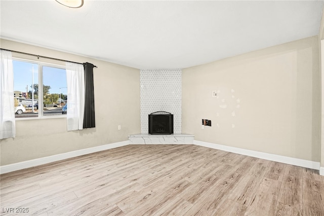 unfurnished living room featuring light wood-style floors, a tile fireplace, and baseboards