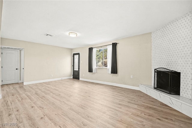 unfurnished living room featuring light wood-type flooring, a tile fireplace, visible vents, and baseboards