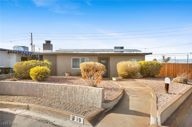 view of front facade with solar panels, a chimney, fence, and stucco siding