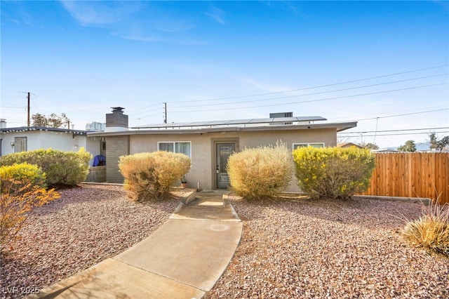 view of front facade with stucco siding, fence, a chimney, and solar panels