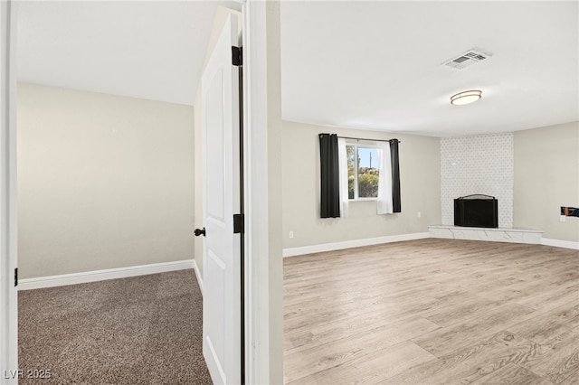 unfurnished living room featuring a large fireplace, light wood-type flooring, visible vents, and baseboards