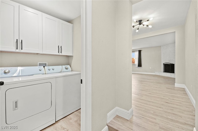 laundry room with baseboards, light wood-type flooring, a brick fireplace, cabinet space, and washer and clothes dryer