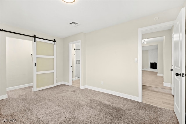 unfurnished bedroom with carpet, a barn door, visible vents, and baseboards